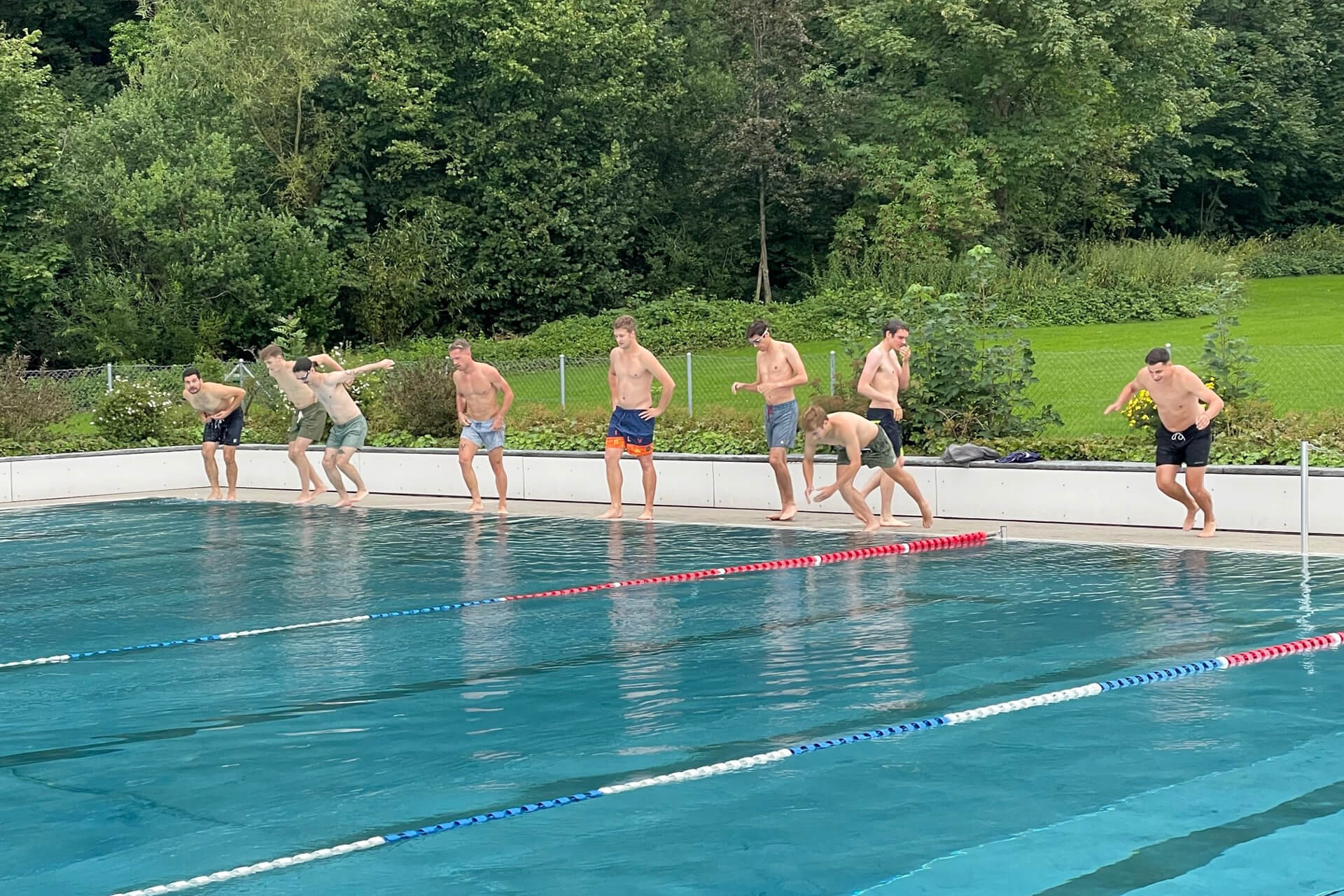 Eine Gruppe von Männern steht am Rand eines Schwimmbeckens.
