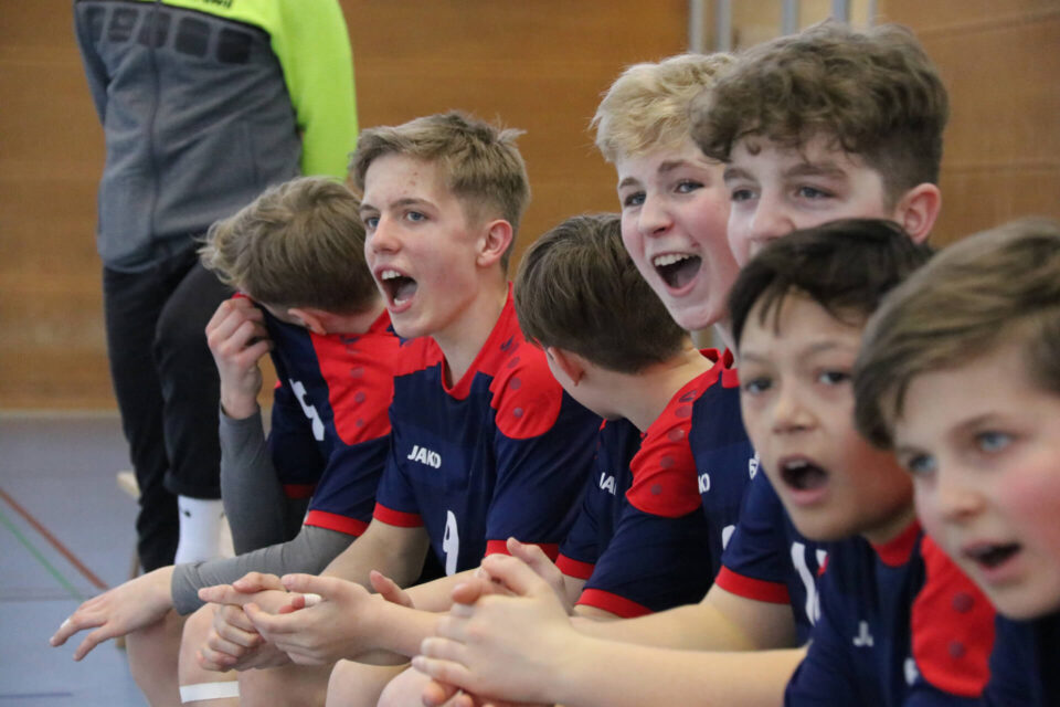 Eine Gruppe Jungen sitzt am Spielfeldrand und feuert Team an.