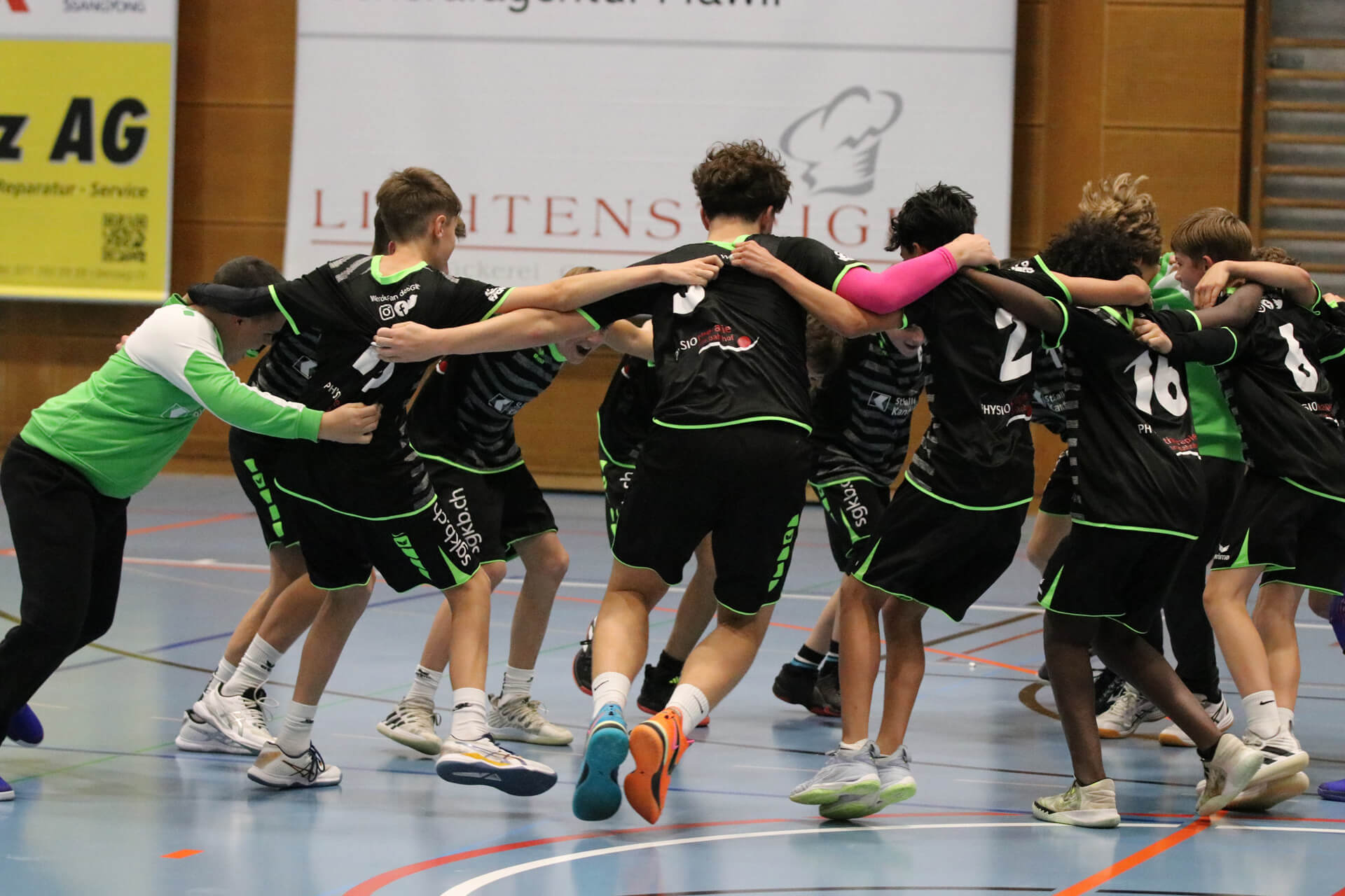 Eine Gruppe Jungen jubelt im Kreis auf einem Spielfeld.